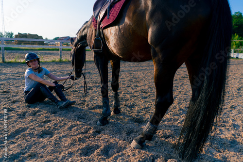 A helmeted rider feeds her beautiful black horse from her hand in the equestrian arena during a horseback ride