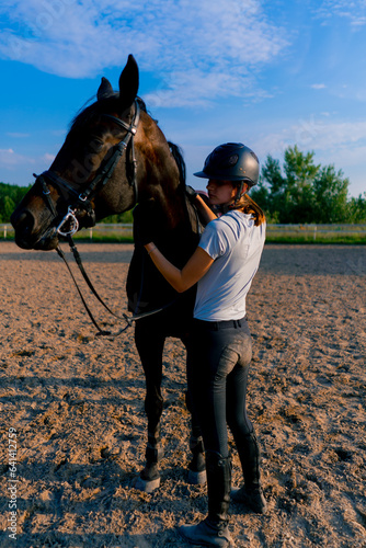 A helmeted rider leads her beautiful black horse by the harness in the riding arena during a horseback ride