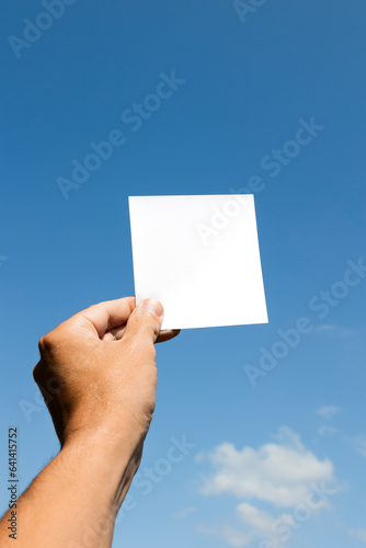 Mão de homem branco segurando papel branco com fundo céu azul