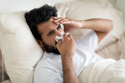 Sick Indian Man Blowing Runny Nose In Napkin While Lying In Bed
