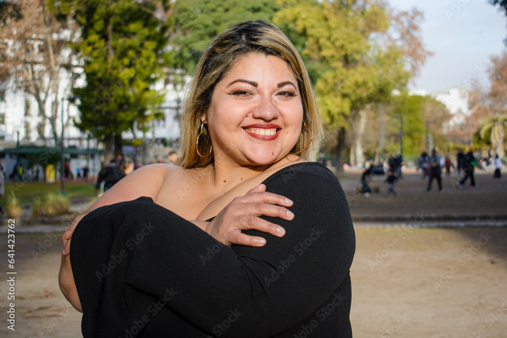 young plus size latina woman standing in park hugging herself showing self love young plus size latina woman standing in park hugging herself showing self love