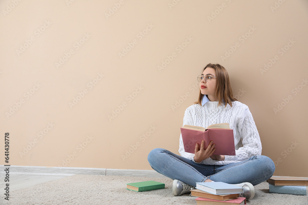Young woman reading book near beige wall Young woman reading book near beige wall