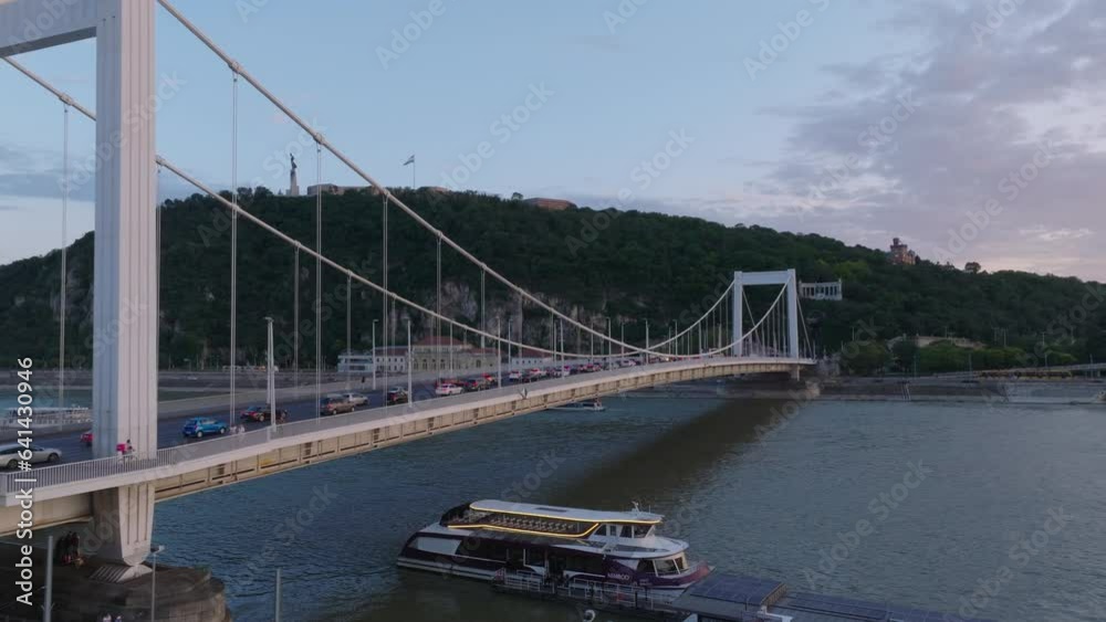 Nice shot of busy road bridge over Danube river. Wooded hill with Citadel and national flag on top in background. Budapest, Hungary