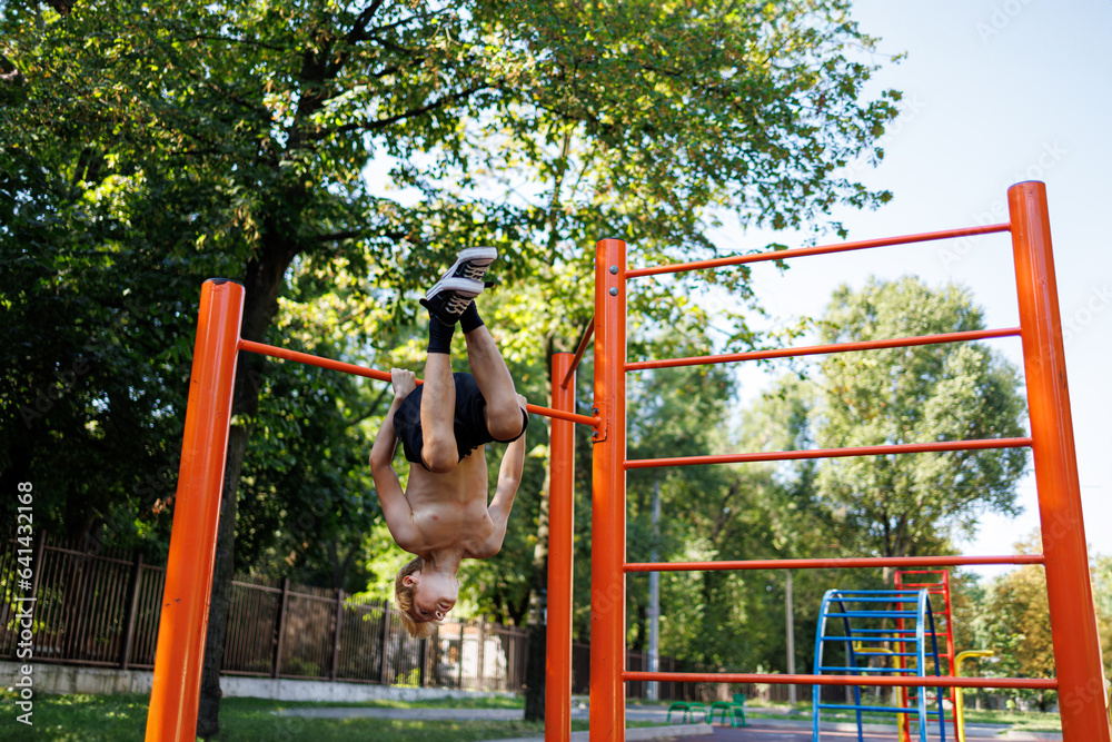 Exercise boy hangs his head down. Street workout on a horizontal bar in the school park.