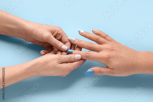 Manicure master applying press-on nail on blue background  closeup