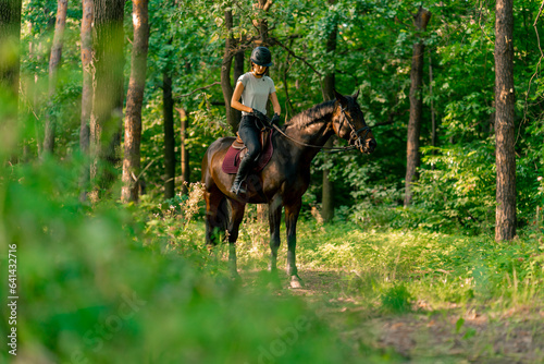 A rider dressed in a helmet rides her beautiful black horse in the forest during a horseback ride © Guys Who Shoot