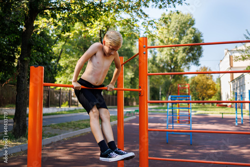 The teenager holds his weight on outstretched arms while performing elements on the crossbar. Street workout on a horizontal bar in the school park.