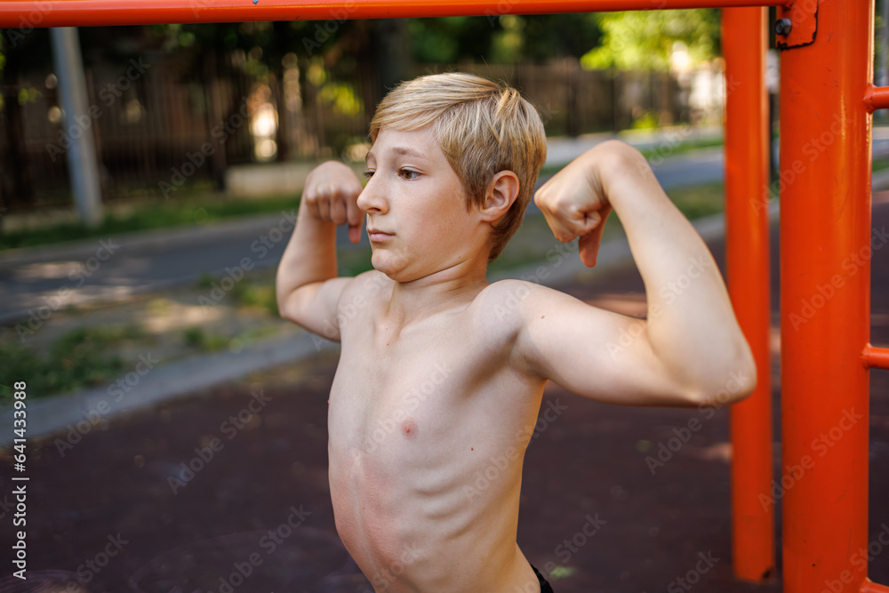 Obraz premium A teenager with an athletic build shows off his musculature. Street workout on a horizontal bar in the school park.