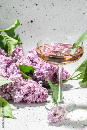 Rose wine in glass with blooming lilac on a light background