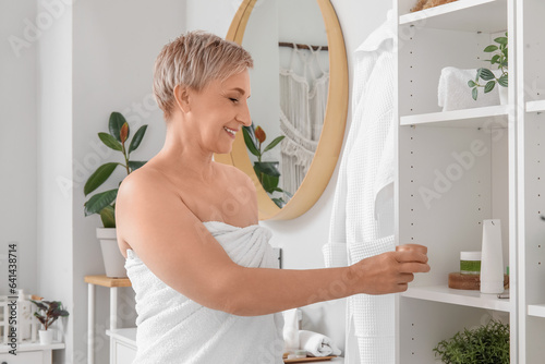 Mature woman taking jar of cream from shelf in bathroom