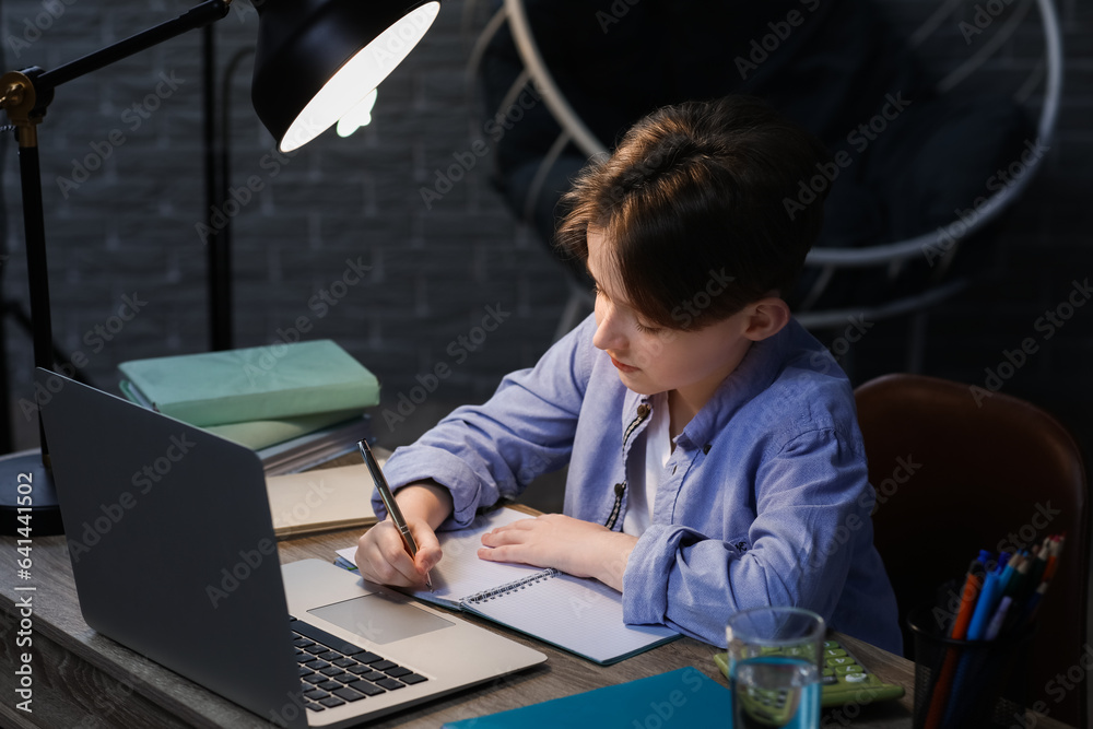 Little boy doing homework with laptop at home late in evening Little boy doing homework with laptop at home late in evening