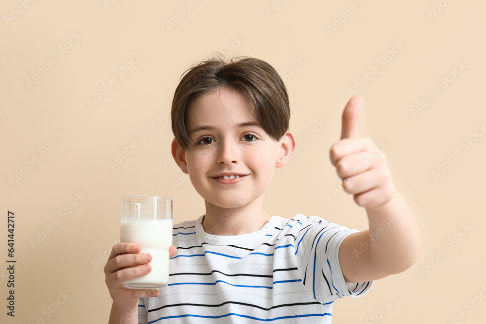 Little boy with glass of milk showing thumb-up gesture on beige background Little boy with glass of milk showing thumb-up gesture on beige background