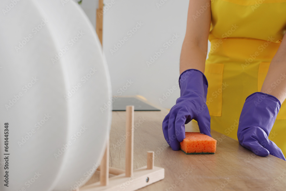 Woman in purple rubber gloves cleaning wooden countertop with sponge