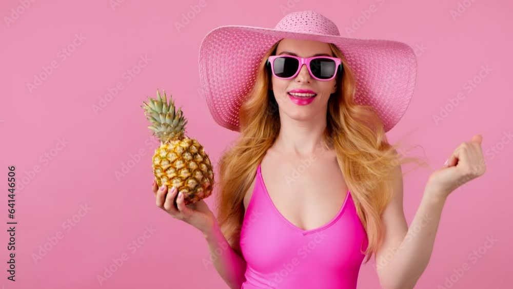 Fashionable woman dancing in swimsuit, total pink, tongue out, hat with pineapple, smiling enjoys summertime for spa, wellness. Playful glamor sexy lady dance, slim body, colorful trend on pink Fashionable woman dancing in swimsuit, total pink, tongue out, hat with pineapple, smiling enjoys summertime for spa, wellness. Playful glamor sexy lady dance, slim body, colorful trend on pink