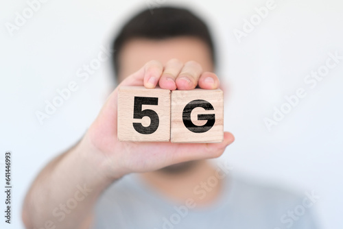 Man holding wooden cubes with 5G text on them, network or communication idea, wooden block cubes with 5G word, blurred man with wood blocks in front of white background, concept banner