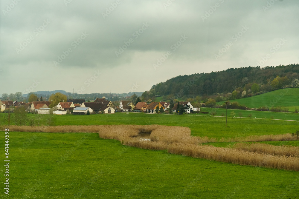 There are rain clouds above the German village, next to the village there is a forest, a field and a pond
