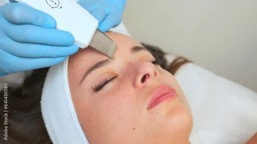Spa worker in rubber gloves cleans face with ultrasonic device. Specialist does cleansing of body part. Smooth skin effect and blemish removal Spa worker in rubber gloves cleans face with ultrasonic device. Specialist does cleansing of body part. Smooth skin effect and blemish removal
