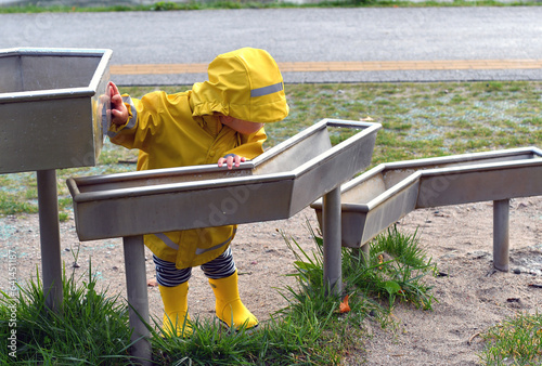  Little boy wearing a yellow raincoat playing on interactive playground.