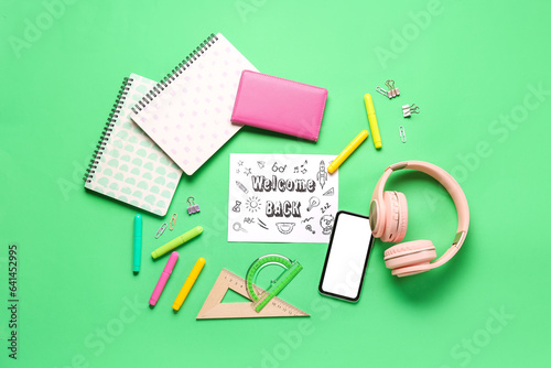 Card with text WELCOME BACK, headphones, stationery and mobile phone on green background