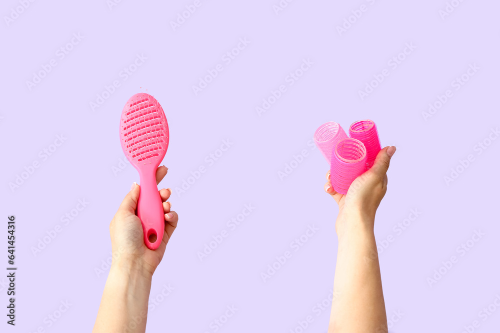 Female hands with curlers and brush on lilac background