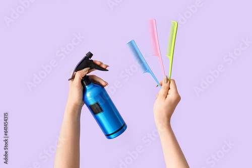 Female hands with hair spray and different combs on lilac background