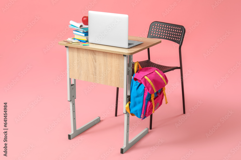 Fototapeta premium Modern school desk with backpack, laptop and stationery on pink background