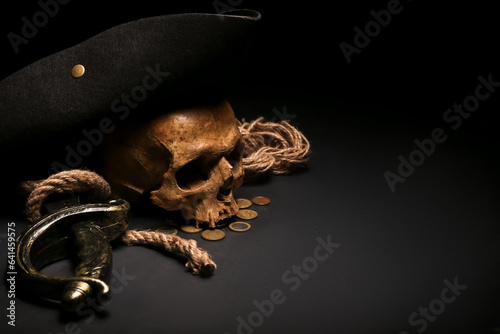 Human skull with sword, toy model of cannon, pirate hat and coins on black background