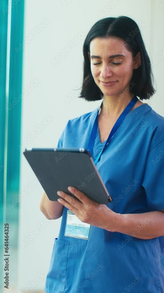 Vertical video portrait of smiling mature female doctor wearing scrubs checking digital tablet in hospital - shot in slow motion Vertical video portrait of smiling mature female doctor wearing scrubs checking digital tablet in hospital - shot in slow motion