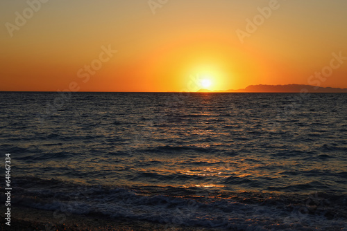 Colorful vibrant orange sunset on the seaside. Golden hour sunlight. Majestic dusk. Seascape in Rhodes  Greece. Reflection of sun path on horizon. Abstract nature and travel background