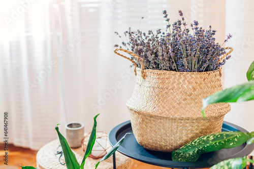 Contemporary boho house decor. Wicker basket filled with lavender bandle on table. Cozy interior in ethnic eco style. photo