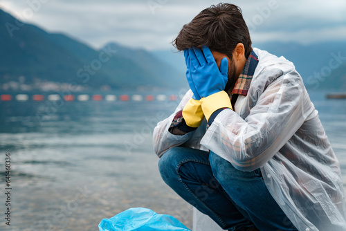 Devastated young man covering eyes with hands while cleaning beach from garbage.