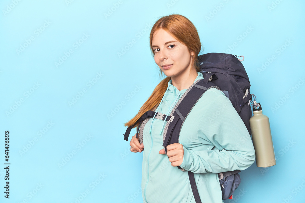 Redhead mountaineer with adventure backpack in blue studio Redhead mountaineer with adventure backpack in blue studio