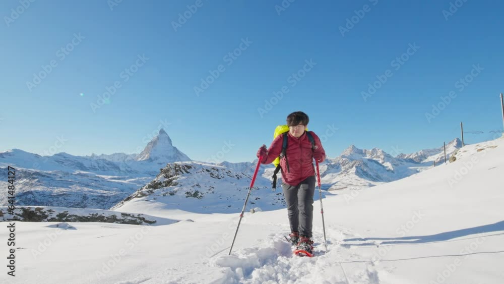 Asian man tourist hiker with backpack walking in snow shoes with famous Matterhorn background. Adventure climber hiking up to swiss alps mountain top. Switzerland travel lifestyle winter activities. Asian man tourist hiker with backpack walking in snow shoes with famous Matterhorn background. Adventure climber hiking up to swiss alps mountain top. Switzerland travel lifestyle winter activities.