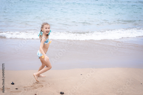 A little girl in a swimsuit runs on a sandy beach in Georgia and plays with the waves
