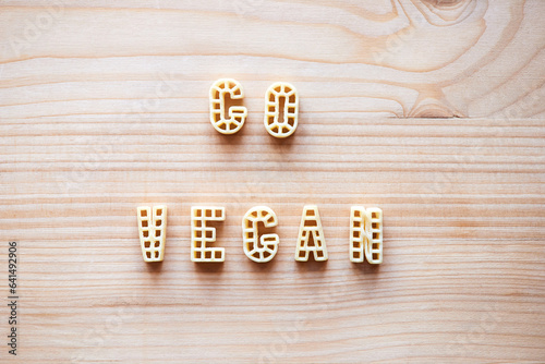 Close-up view of alphabet pasta forming lettering ‘Go vegan’ on wooden table  photo