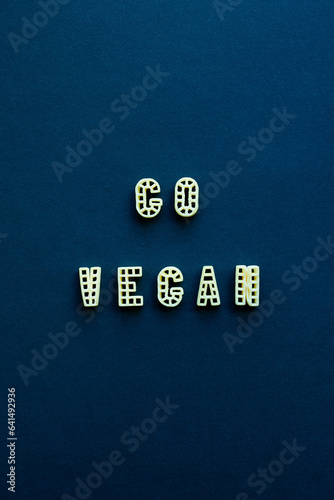 Alphabet pasta forming inspirational lettering ‘Go vegan’ against dark blue background  photo