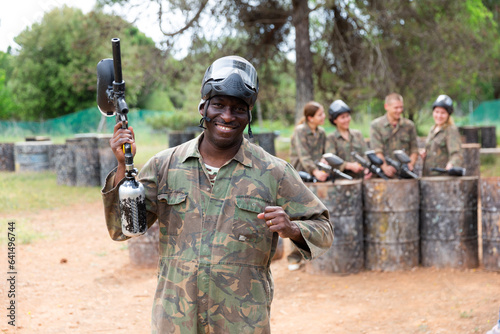 Portrait of paintball player in camouflage and protective mask standing with gun after paintball match outdoors
