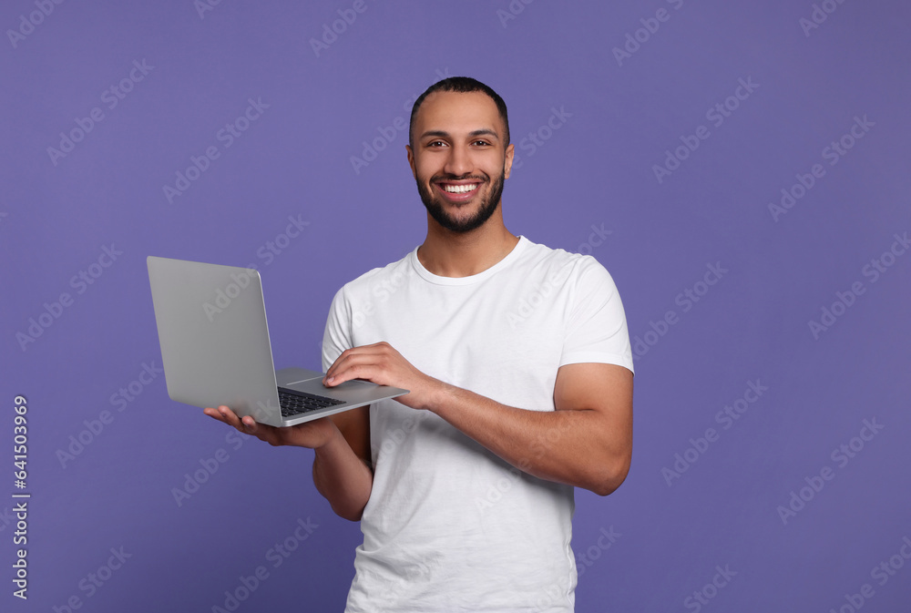 Smiling young man working with laptop on lilac background Smiling young man working with laptop on lilac background