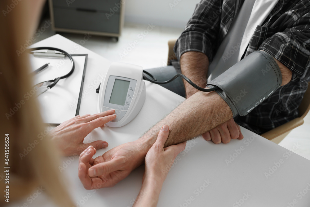 Doctor measuring blood pressure of man at table indoors, closeup