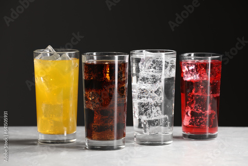 Glasses of different refreshing soda water with ice cubes on white marble table