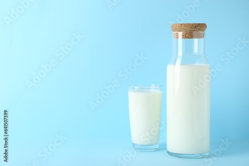 Carafe and glass of fresh milk on light blue background, space for text