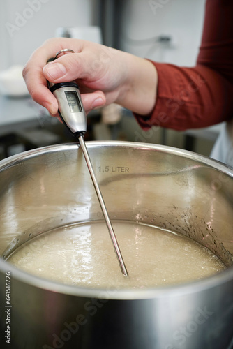 Close-up view of unrecognizable female cook measuring temperature of melting sugar in saucepan with modern kitchen thermometer  photo