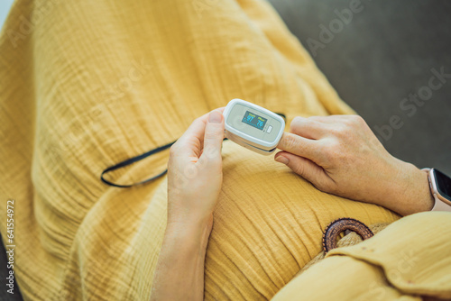 Obraz na płótnie Pregnant woman with pulse oximeter on finger. Doctor measuring oxygen saturation level while visiting expectant mother with coronavirus disease at home, cropped. Pregnancy and covid-19 concept w salonie