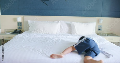 Happy asian 5 year boy jump and rolling on hotel bed while summer vacatioin trip enjoy summer recreation  photo