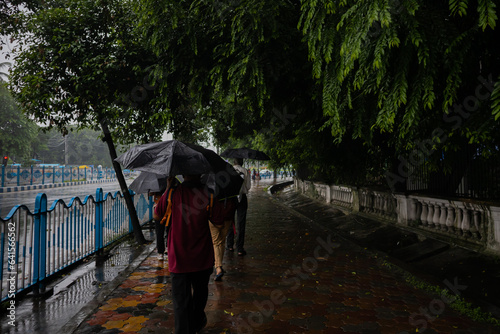 people walking with umbrella on a rain wet foot path and during monsoon season in streets of kolkata india. 