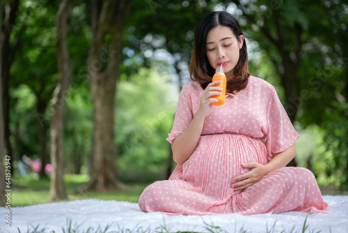 Portrait of Asian pregnant woman relaxing and drinking orange juice in the park