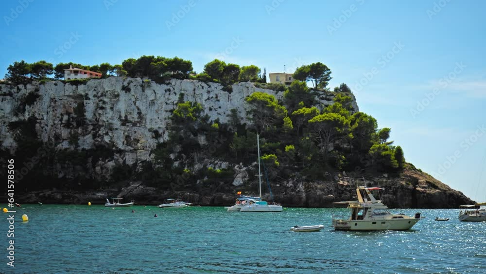 People relax by the Mediterranean Sea sailing and staying at the rocky cave beach. Boats and vessels with tourists having good time in Cala Galdana on the Island of Menorca, Balearic Islands, Spain People relax by the Mediterranean Sea sailing and staying at the rocky cave beach. Boats and vessels with tourists having good time in Cala Galdana on the Island of Menorca, Balearic Islands, Spain