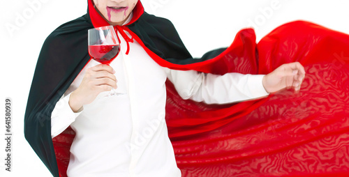 Close up and motion blur image of Asian man wearing Halloween costume as witch in red cloak, on white background, Dracula holding red wine glass, looking at camera