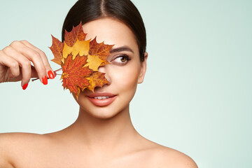 Portrait of beautiful young woman with autumn leafs. Healthy clean fresh skin natural make up beauty eyes and red nails