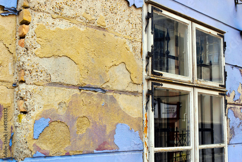 grunge spalling stucco elevation and old wood window. rusty hinges and metal corner plates. damaged facade. lack of maintenance concept.  photo